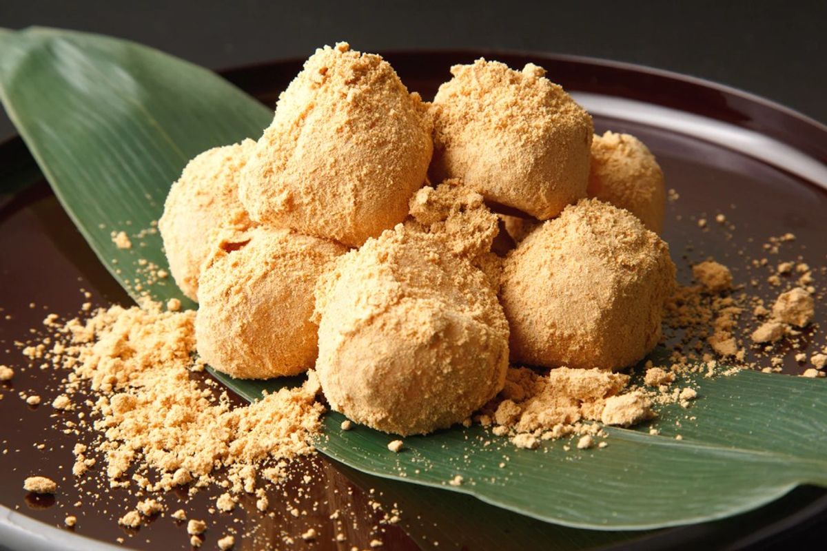 Kinako mochi balls dusted with soybean powder on dark plate with green leaves
