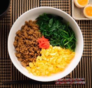 Bibimbap bowl with ground meat, spinach, egg, pickled radish, and rice on woven placemat