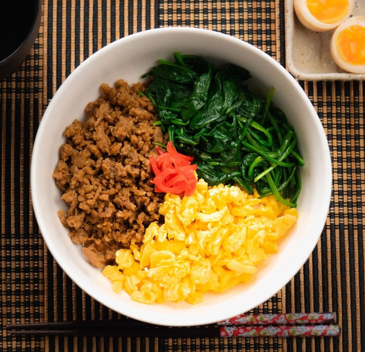 Bibimbap bowl with ground meat, egg, spinach, pickled radish, and rice on woven placemat