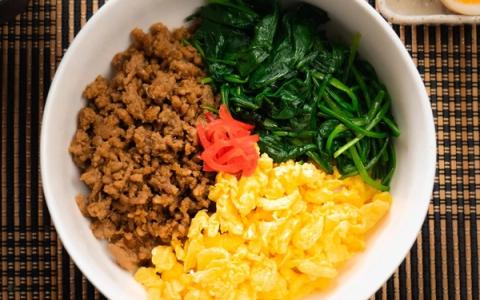 Bibimbap bowl with ground meat, spinach, egg, pickled radish, and rice on woven placemat
