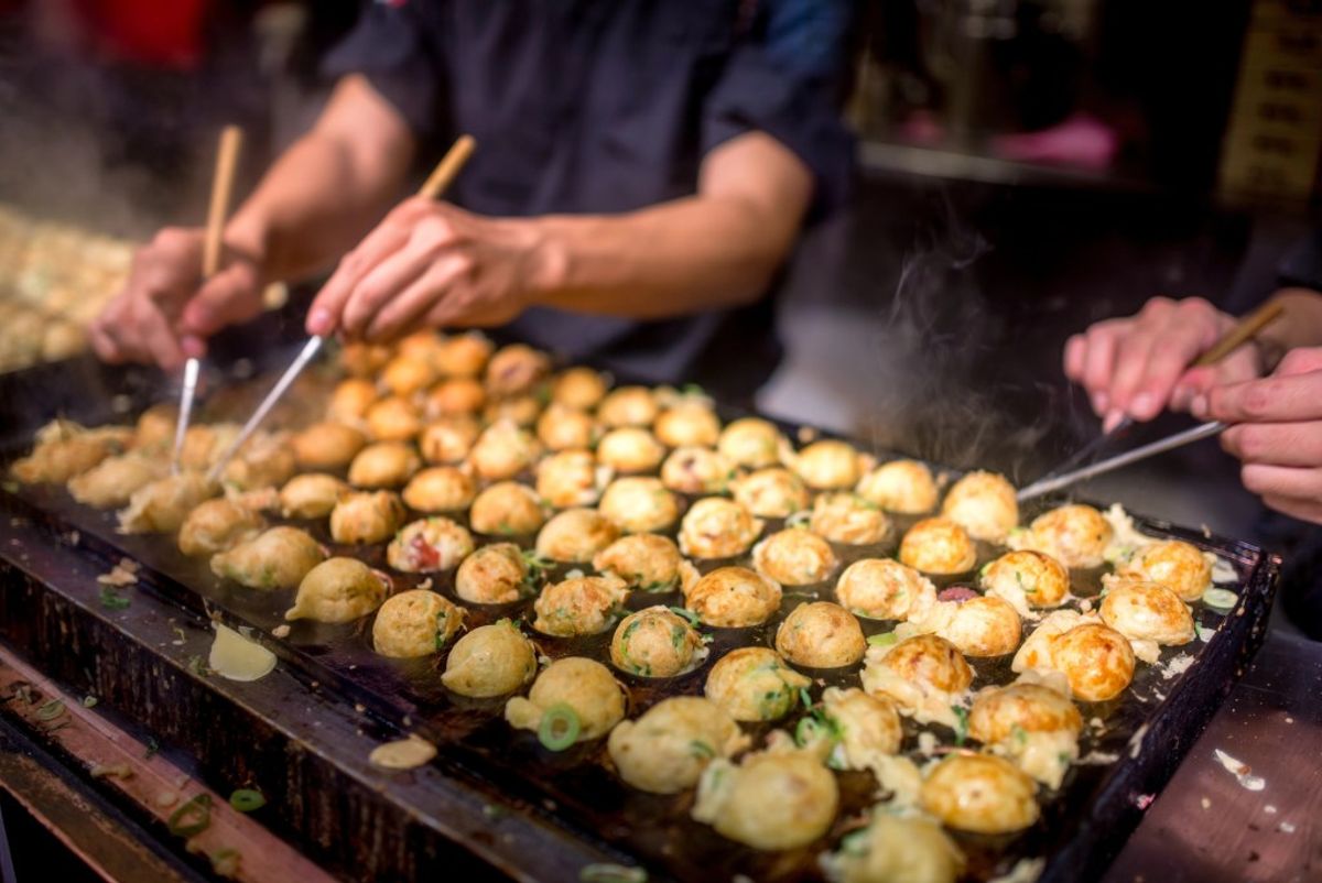 Street vendor preparing takoyaki balls on griddle with chopsticks, steam rising
