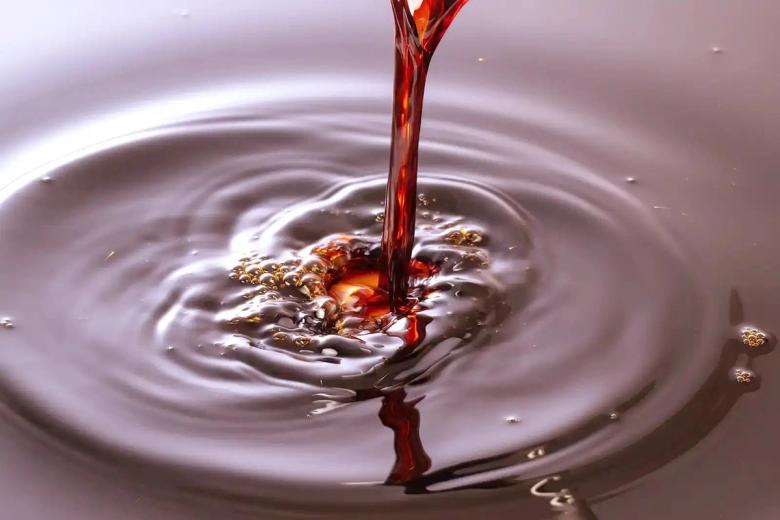 Red liquid splashing into water creating ripples and dynamic waves on surface