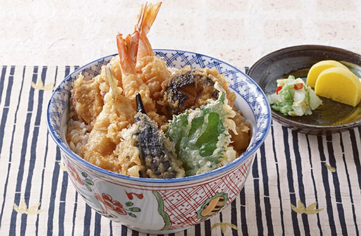 Tempura donburi bowl with shrimp, vegetables, and dipping sauce on striped placemat