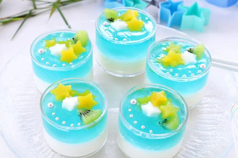 Five layered gelatin desserts with turquoise blue jelly, white cream, star-shaped fruit garnish, and pearl decorations