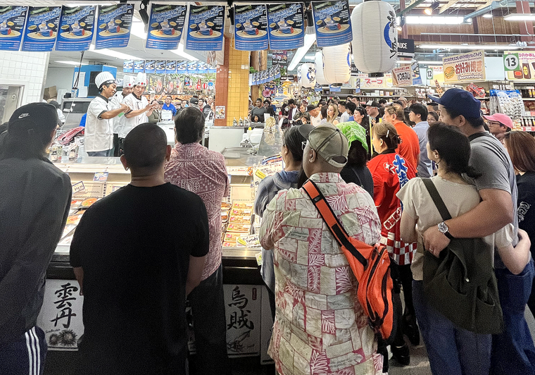 Crowded Japanese fish market counter with vendors serving customers during busy daytime hours