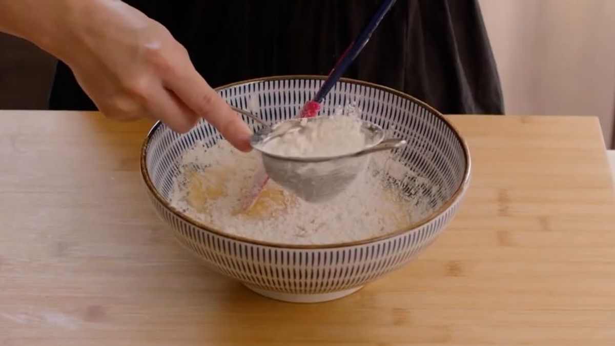 Person sifting flour into bowl with whisk for baking preparation