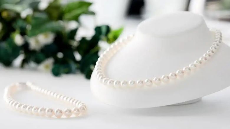 Pearl necklace and bracelet displayed on white mannequin with white flowers in background