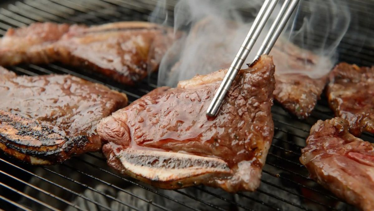 Grilled beef steaks sizzling on barbecue grill with tongs, showing charred surface and juices