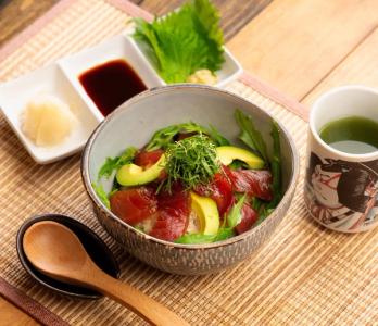 Maguro don with avocado, cucumber, and garnish in ceramic bowl with condiments