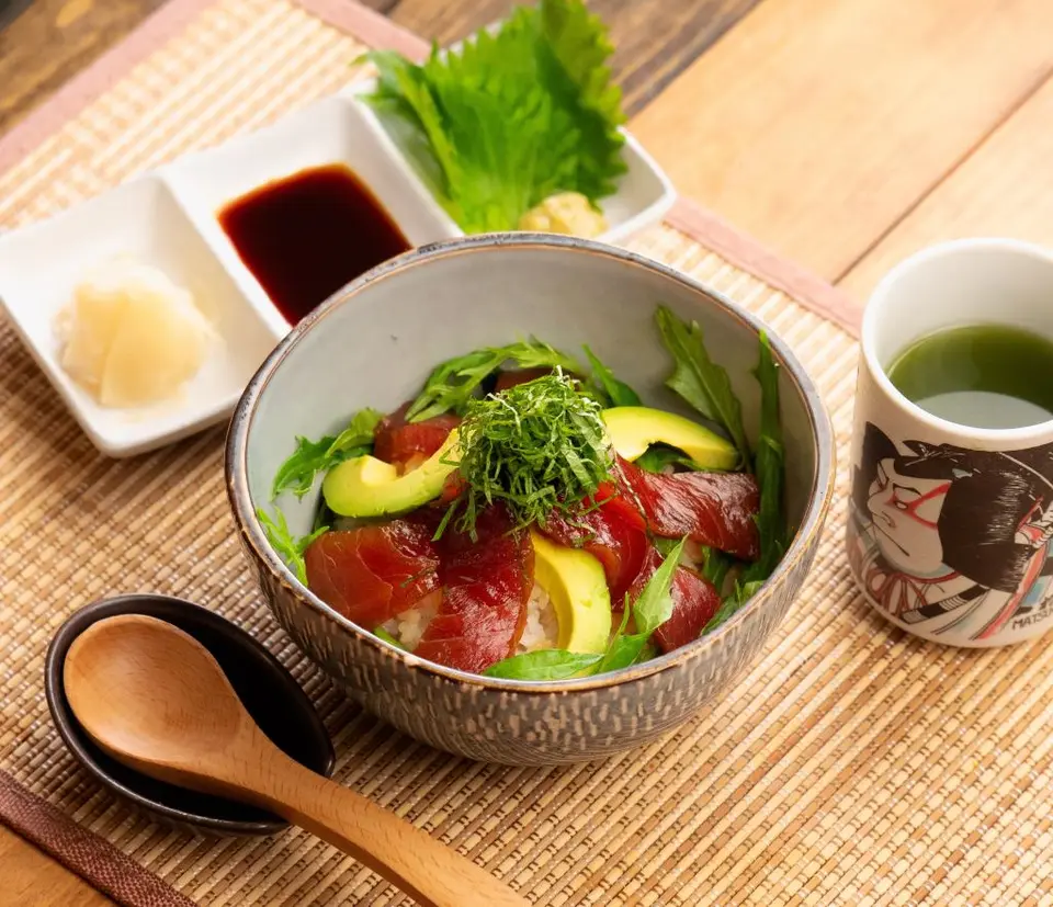 Maguro don with avocado, cucumber, and garnish in ceramic bowl with condiments