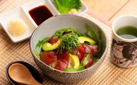 Maguro don with avocado, cucumber, and garnish in ceramic bowl with condiments