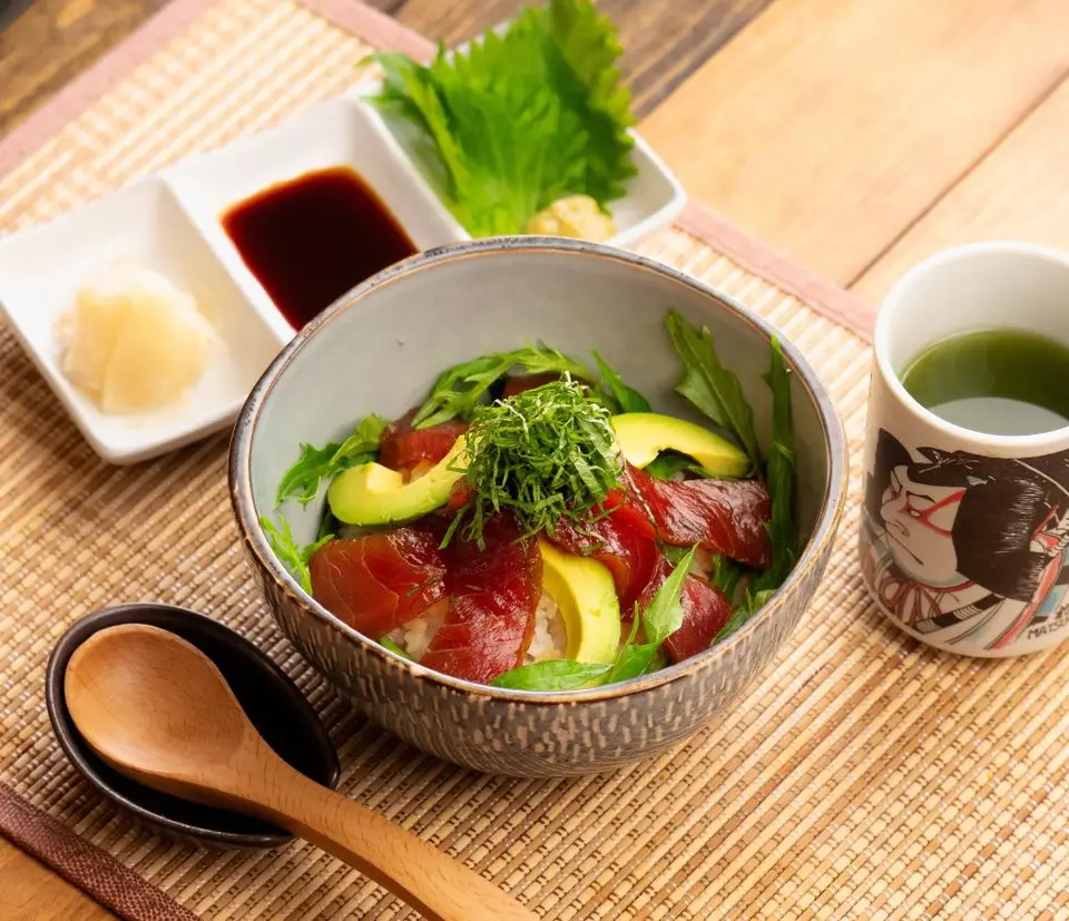 Maguro don with avocado, cucumber, and garnish in ceramic bowl with condiments