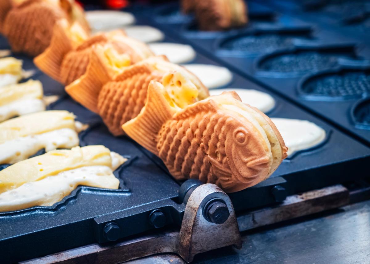 Fish-shaped taiyaki pastries in mold with white filling and metal tongs