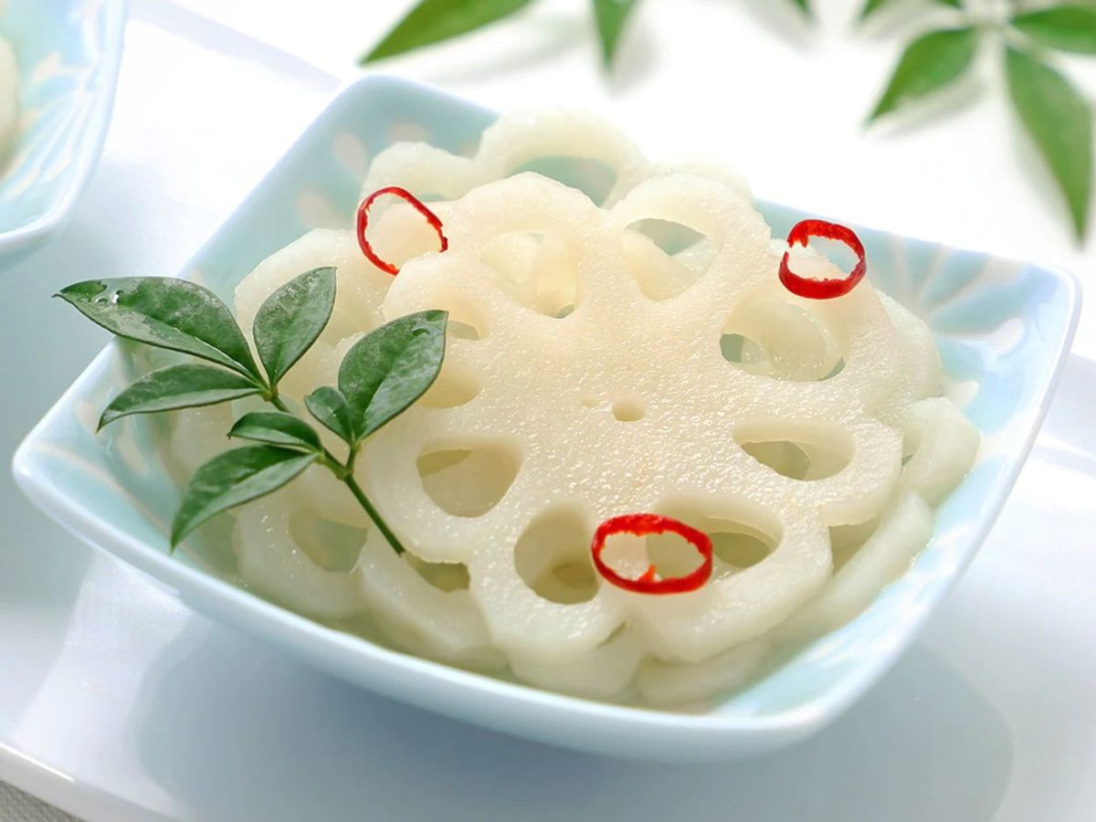 Sliced lotus root with red chili peppers and herb garnish on white plate