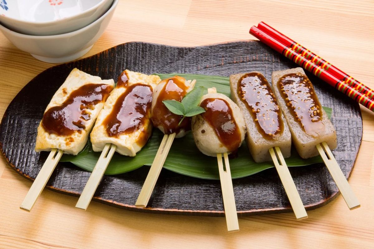 Six dango skewers with glazed topping arranged on dark plate with green leaf garnish