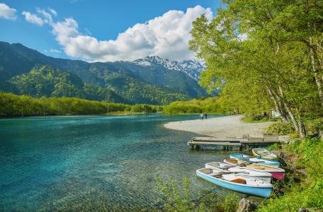 Alpine lake with turquoise water, rowboats, sandy beach, snow-capped mountains, forest