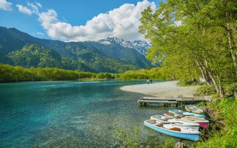 Alpine lake with turquoise water, rowboats, sandy beach, snow-capped mountains, forest