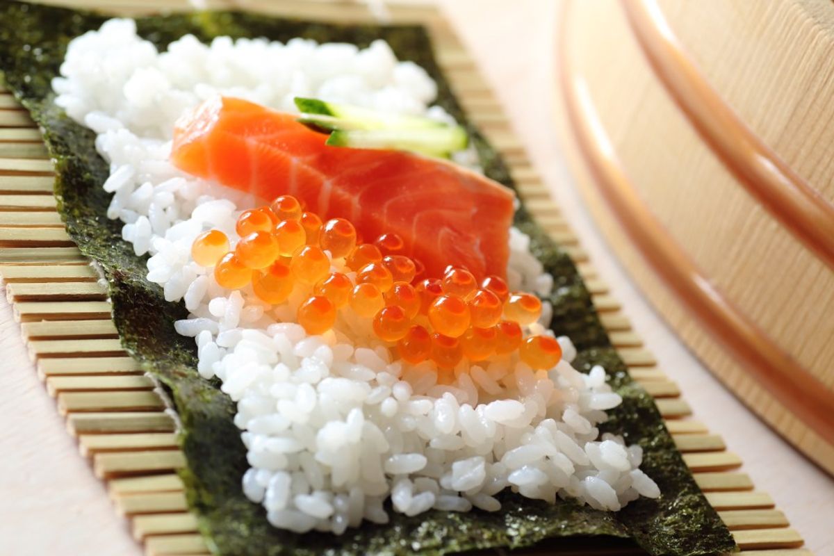 Nigiri sushi with salmon and ikura on nori, bamboo mat, wooden bowl visible