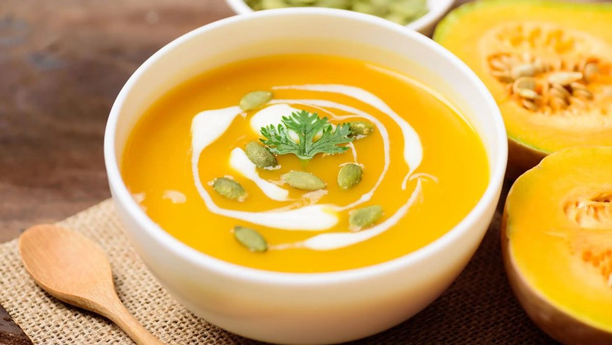 Butternut squash soup garnished with cream, pumpkin seeds, and fresh parsley in white bowl