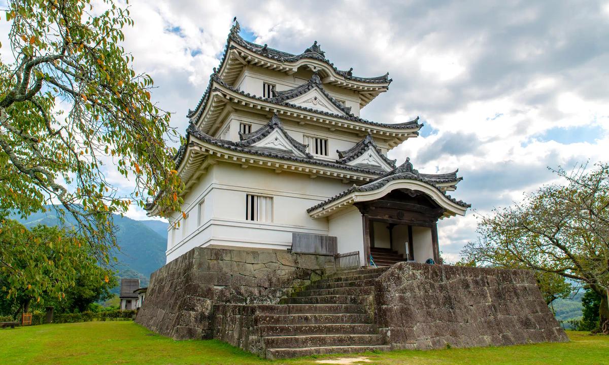 Traditional Japanese castle with multiple tiered roofs, stone foundation, surrounded by green landscape