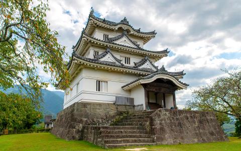 Traditional Japanese castle with multiple tiered roofs, stone foundation, surrounded by green landscape