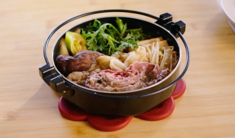 Hot pot with broth, beef, noodles, vegetables, and mushrooms on wooden table