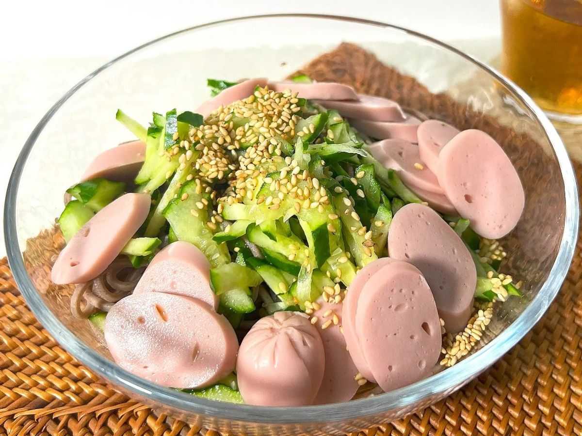 Glass bowl of cucumber salad with sliced pink fish cake and sesame seeds