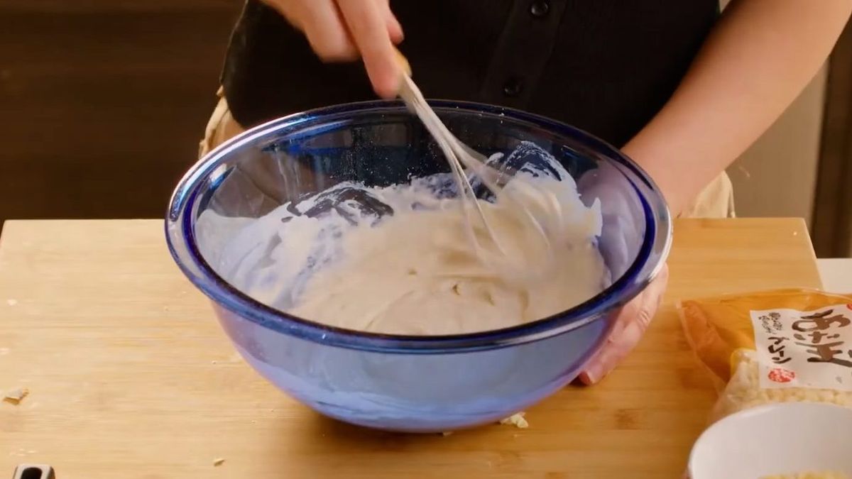 Person stirring whipped cream or mayonnaise in blue mixing bowl with spatula