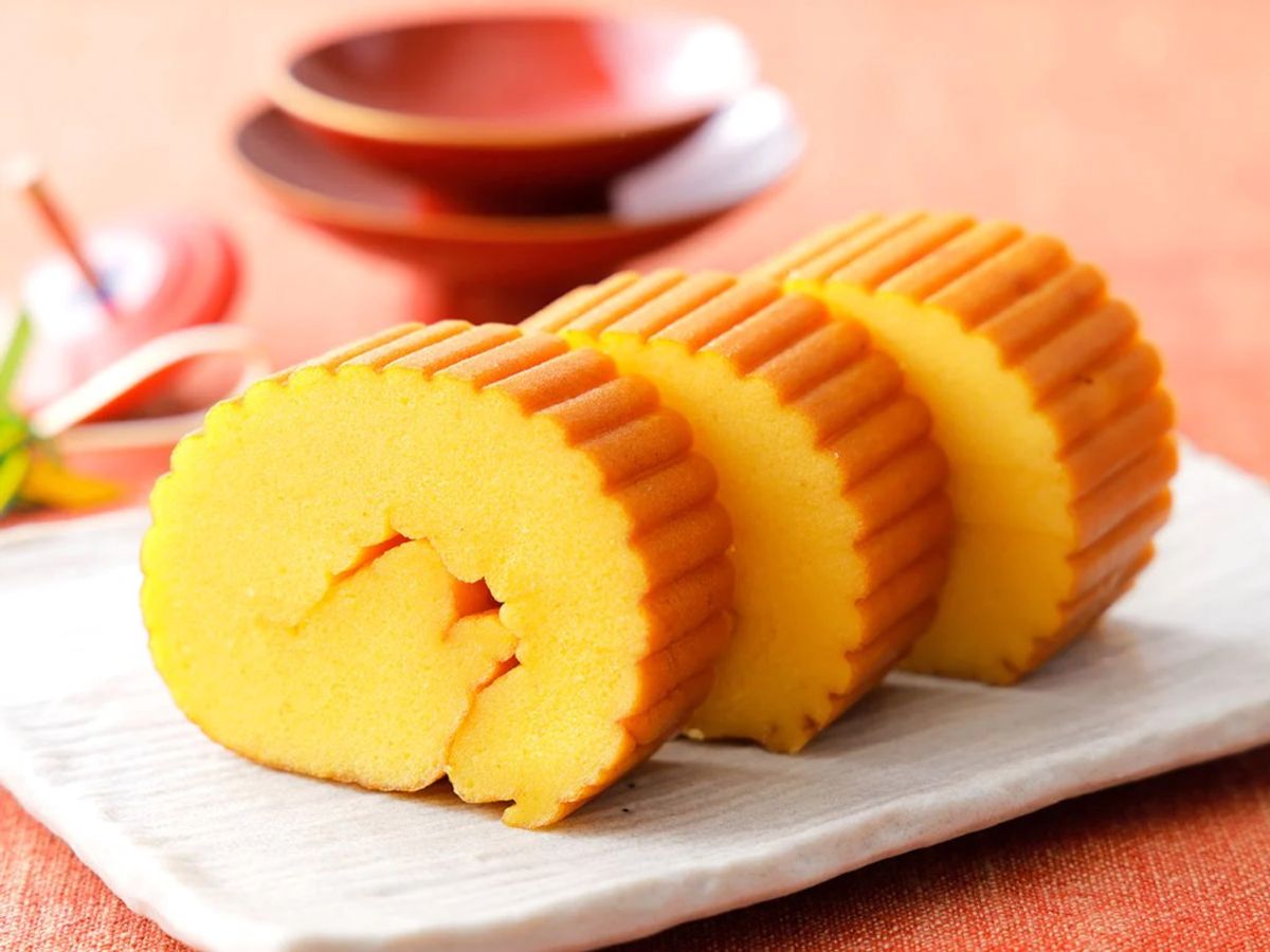 Yellow sponge cake with ridged edges sliced on white plate, peach background