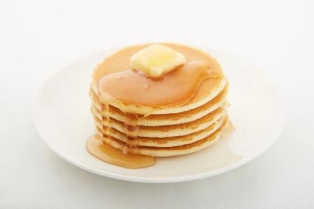 Stack of golden pancakes with butter and syrup on white plate