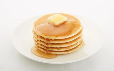 Stack of golden pancakes with butter and syrup on white plate
